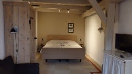 kamer met een tweepersoonsbed in B&B 't Kraaijenest in Midden-Delfland met een grijze houten deur, witte balken