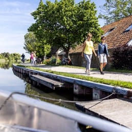 fietser en wandelaars langs de Vlaardingsevaart op een zonnige dag met water in de voorgrond en rechts de fietsers en wandelaars op het pad langs het water ter hoogte van B&B rechthuis van Zouteveen