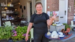 Marga van der Wulp van Galeri Weerloos staat voor haar galerie met Scandinavisch design met een dienblad met thee en gebak gemaakt van 100% biologische producten uit de streek Midden-Delfland