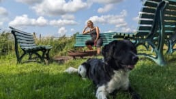 Angela van Buitengoed Ta Fête op een groen bankje bij de vuurplaats op de rand van de camping met hond Guus