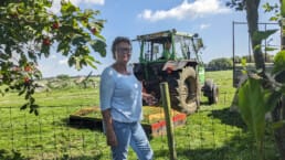 Anjo Vonk uit Vlaardingen staat bij een hek bij Camping Bouwlust in Midden-Delfland met op de achtergrond een tractor met de boer die gras aan het maaien is