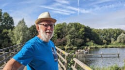 Aart van Dijk met blauw t-shirt en hoedje op langs het water van de Vlaardingse vaart voor de column Midden-Delfland door de ogen van