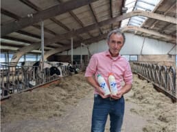 boer Arnold van Adrichem met 2 flessen zuivel van Delflandshof in een stal met koeien in Midden-Delfland maker streekproduct zuivel melk yoghurt