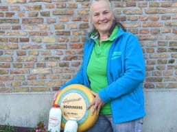 boerin Nelly van Winden van Kaas- en Zuivelboerderij van Winden met een kaas en twee flessen melk en yoghurt zuivel gemaakt in Midden-Delfland makers boeren