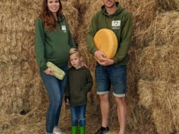 Roel van Buuren met zijn vrouw Femke en zoontje Levi in een schuur met hooi en een grote ronde gele kaas en een doosje eieren van hun Boerderij Landlust in Midden-Delfland boer maker streekproducten