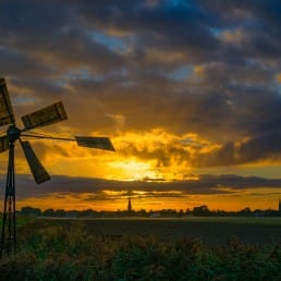 weide met opkomende zon en wolken met een windmolen in Midden-Delfland