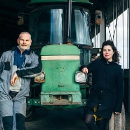 Pauline Schouwenburg met Johan Oosthoek boer in Midden-Delfland poseren voor een traktor in een schuur met koeien in Midden-Delfland